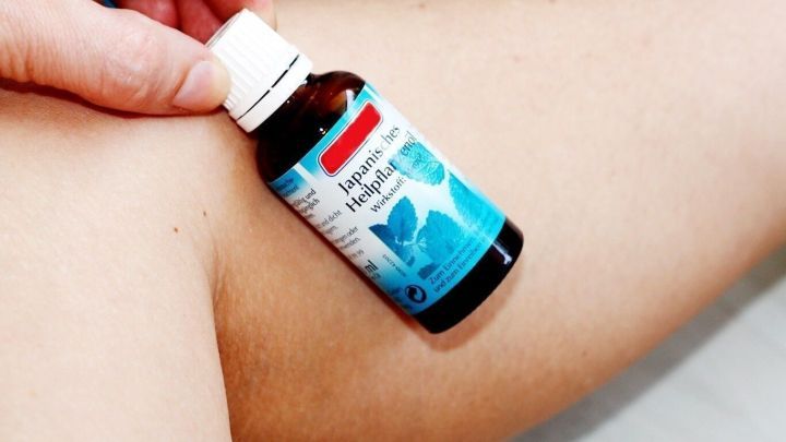 Eine Hand h&auml;lt eine Flasche JHP, w&auml;hrend diese auf einen schmerzenden Oberschenkel aufgetragen wird, um Muskelkater zu lindern.