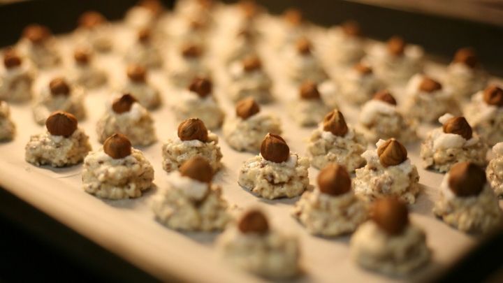 Kleine Haselnussmakr&ouml;nchen auf einem Blech, die gleich gebacken werden, umgeben von einer warmen K&uuml;chenszene.