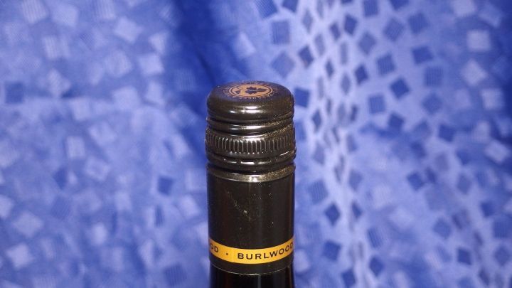 Eine Flasche Wein mit schwarzem Korken steht vor einem blauen, gemusterten Hintergrund, bereit zum &Ouml;ffnen.