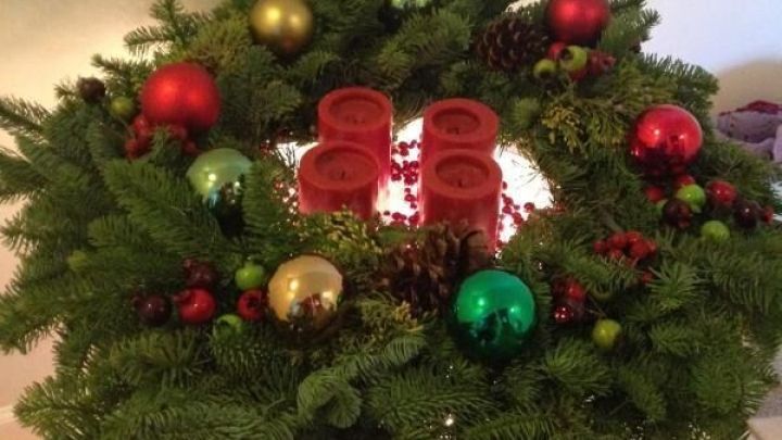 Adventskranz mit roten Kerzen und bunten Kugeln steht auf einem Tisch in einem Raum mit gefliesten Boden.