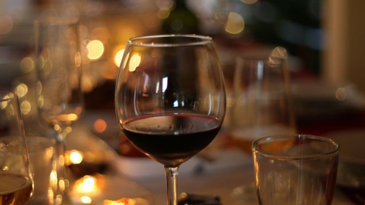 Ein Rotweinglas steht auf einem eleganten Tisch. Bei Kerzenlicht genie&szlig;en G&auml;ste eine festliche Atmosph&auml;re in einem Restaurant.