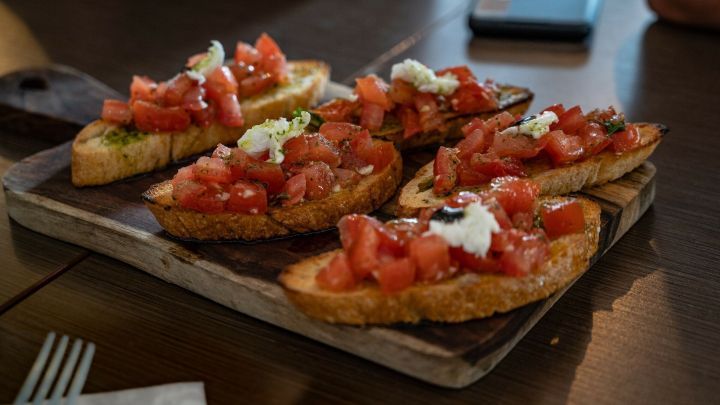 Krosse Bruschetta liegen auf einem Holzbrett, belegt mit frischen Tomaten und Kr&auml;utern, bereit zum Genie&szlig;en.
