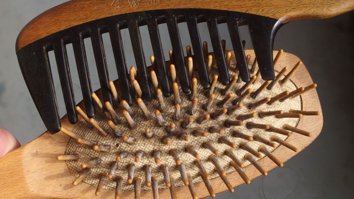 Eine Haarb&uuml;rste mit Haaren wird in einer Hand gehalten, w&auml;hrend sie gereinigt wird, im neutralen Hintergrund sichtbar.