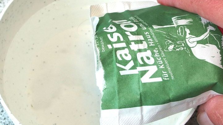 Eine Hand h&auml;lt eine T&uuml;te mit Natron &uuml;ber eine Sch&uuml;ssel mit Wasser, um damit die H&auml;nde zu reinigen.