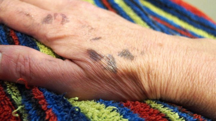 Eine Hand mit Farbflecken liegt auf einem bunten Handtuch und zeigt die Auswirkungen von Haart&ouml;nung auf der Haut.