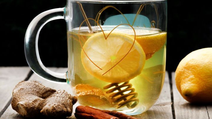 Ein Glas Ingwer-Gl&uuml;htee mit Zitronenscheiben und Zimtstangen steht auf einem Holztisch, umgeben von frischer Zutat.