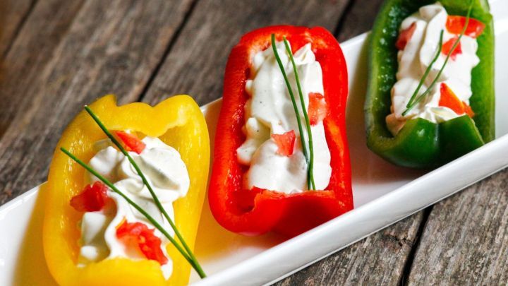 Paprikah&auml;lften gef&uuml;llt mit einer wei&szlig;en Creme und dekoriert mit Schnittlauch liegen auf einer l&auml;nglichen wei&szlig;en Platte.