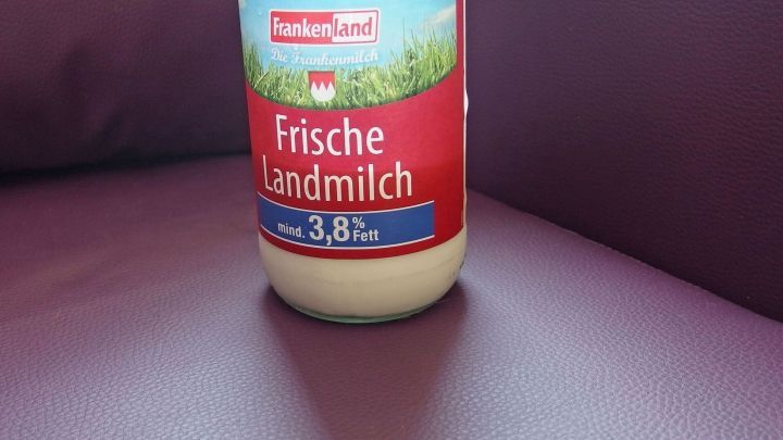 Ein Flasche frische Landmilch steht auf einem glatten, lila Ledersofa, bereit zur Pflege und Reinigung des Sofas.