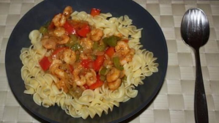 Auf einem Teller befinden sich Nudeln, die mit einer bunten Mischung aus Schrimps, Paprika und Sellerie serviert werden.