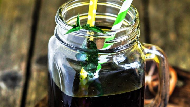 Ein Glas mit dunklem &Ouml;l steht auf einem Holzbrett, w&auml;hrend zwei bunte Strohhalme darin stecken.