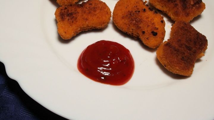 Kross gebratene Nuggets liegen auf einem wei&szlig;en Teller, umgeben von einer Portion hausgemachter S&uuml;&szlig;sauer-Sauce.