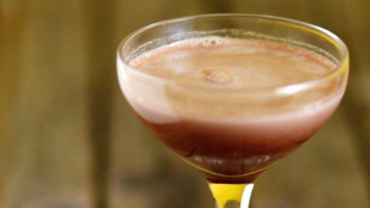 Ein elegantes Glas mit Pfefferminz-Schokoladent&auml;felchen-Lik&ouml;r steht auf einem rustikalen Holztisch, neben zwei Schokoladent&auml;felchen.