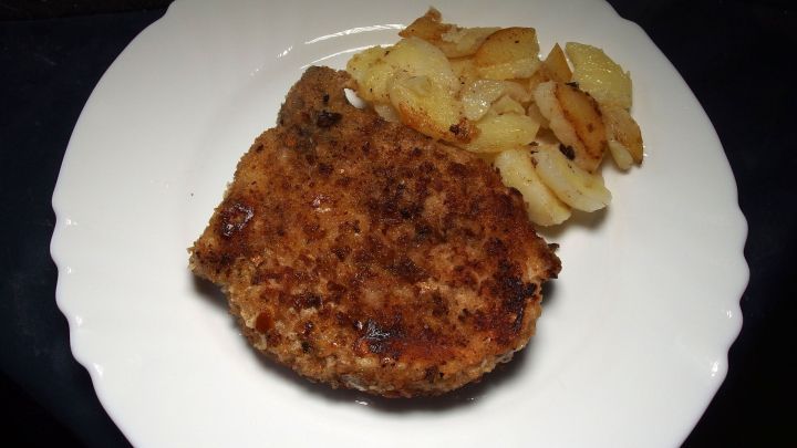 Das goldbraun gebratene M&uuml;nchner Schnitzel liegt auf einem wei&szlig;en Teller neben knusprigen Kartoffelst&uuml;cken.