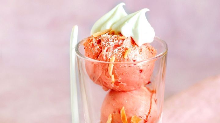 Sch&auml;lchen mit Low-Carb-Fruchteis, dekoriert mit Sahne und eine Erdbeere, auf einem rosa Tischcloth.