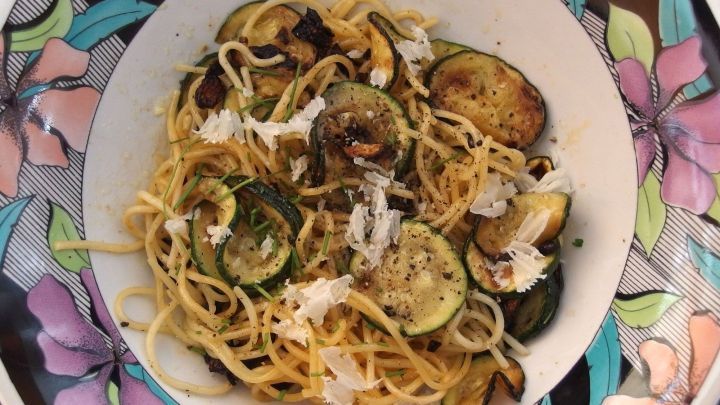 Eine Sch&uuml;ssel Spaghetti mit Zucchini wird mit ger&ouml;stetem Gem&uuml;se und K&auml;se auf einem bunten Teller serviert.