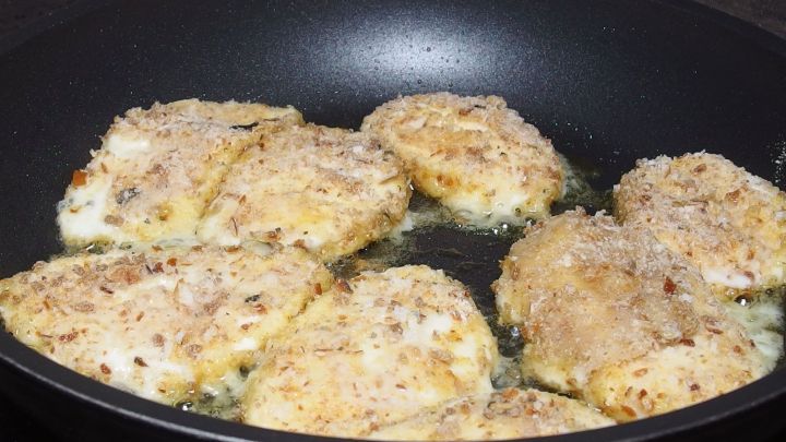 Gebackener Mozzarella br&auml;t in einer Pfanne, w&auml;hrend seine goldene Kruste knusprig wird und im hei&szlig;en &Ouml;l zischend brutzelt.