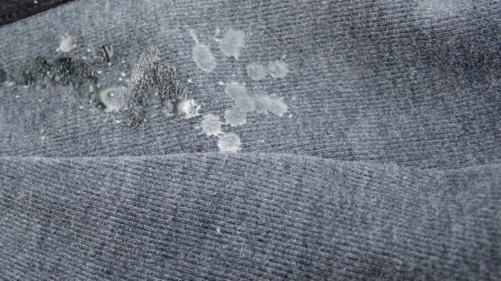 Ein graues Kleidungsst&uuml;ck liegt auf einer Oberfl&auml;che, mit mehreren Wachsflecken, die entfernt werden sollen, m&ouml;glicherweise mit Orangen&ouml;l.