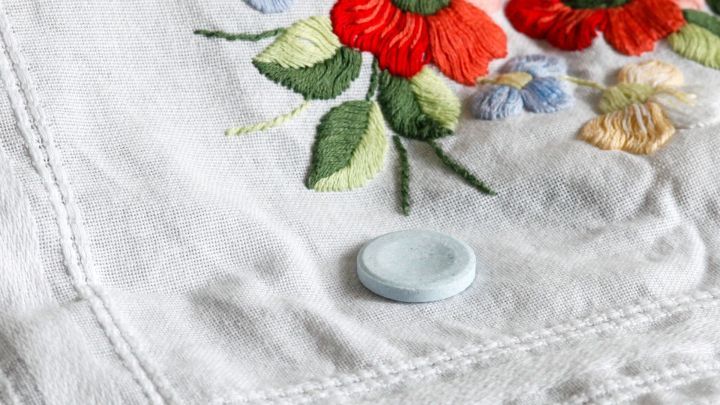 Eine blaue Tablette liegt auf einem gestickten, blauen Stoff mit bunten Blumenmotiven, ideal zur Fleckentfernung.
