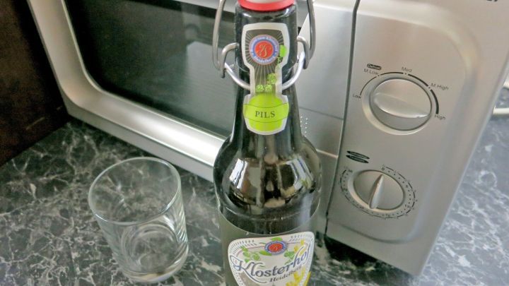 Bierflasche steht neben leerem Glas auf einer Marmoroberfl&auml;che, direkt vor einem TechnoStar-Mikrowellenofen.