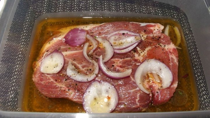 Eine mariniertes Kammsteak liegt in einer durchsichtigen Sch&uuml;ssel mit Zwiebelringen und einer w&uuml;rzigen Marinade.