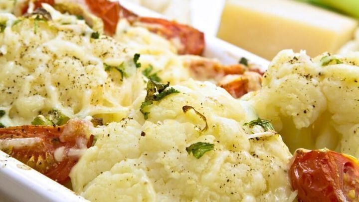Ein goldener Blumenkohlauflauf mit Tomaten und K&auml;se, serviert in einer wei&szlig;en Auflaufform, liegt appetitlich bereit.