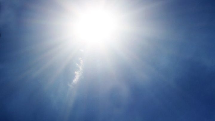 Sonne strahlt hell am blauen Himmel, umgeben von d&uuml;nnen Wolkenschleiern.