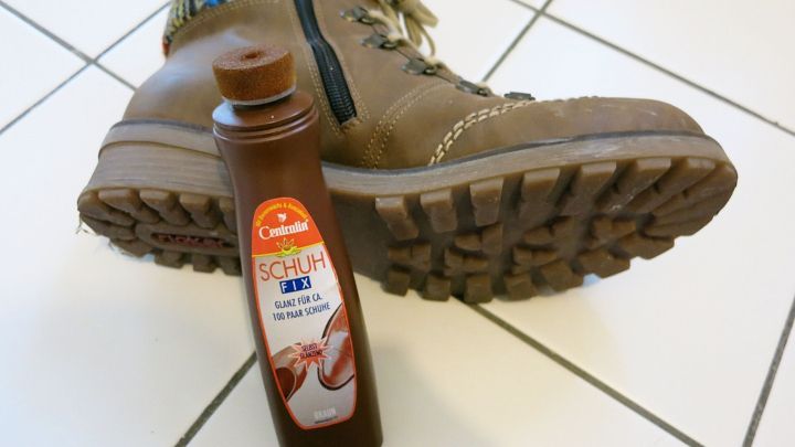 Ein Paar Wildlederschuhe liegt neben einer Flasche, die zur Pflege und Umwandlung in Glattleder genutzt wird.