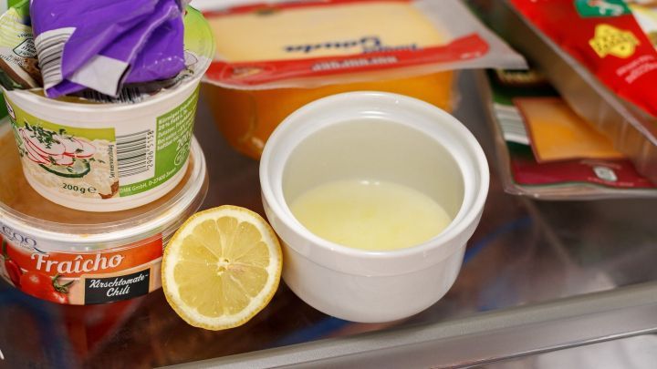Ein Beh&auml;lter mit einer gelben Fl&uuml;ssigkeit steht neben einer halbierten Zitrone im K&uuml;hlschrank, um unangenehme Ger&uuml;che zu neutralisieren.