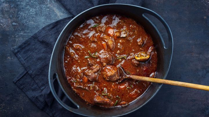 Ein gro&szlig;er Topf mit aromatischem Eintopf kocht in einer dunklen Umgebung, w&auml;hrend ein Holzl&ouml;ffel darin r&uuml;hrt.