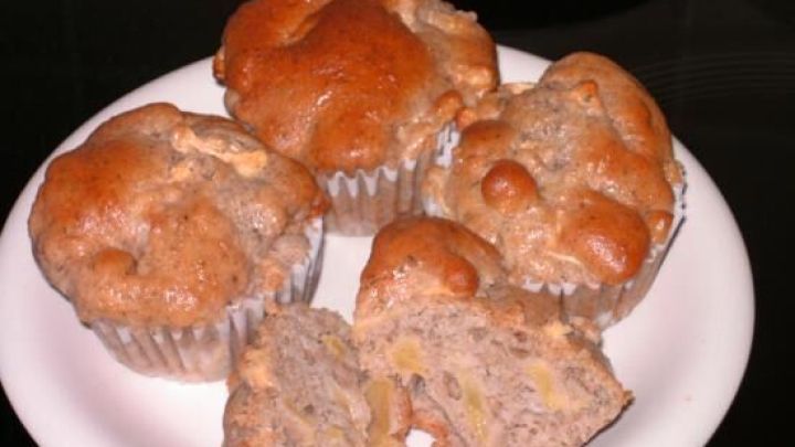 Auf einem Teller ruhen vier goldbraune Bananenmuffins; einer ist halbiert, zeigt saftige Bananenst&uuml;cke.