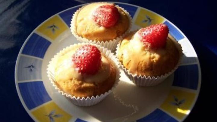 Drei Erdbeer-Muffins auf einem bunten Teller, garniert mit Erdbeeren, im Sonnenlicht auf einem Tisch. Text: 01.05.2009 Nachi.