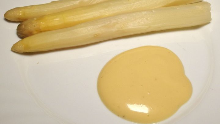 Wei&szlig;e Spargelstangen liegen neben einer gelben So&szlig;e auf einem Teller und zeigen die Kombination zum Essen.