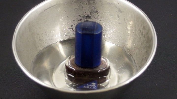 Ein Nagellackfl&auml;schchen steht in einem Wassergemisch in einer silbernen Sch&uuml;ssel, um es wieder fl&uuml;ssig zu machen.