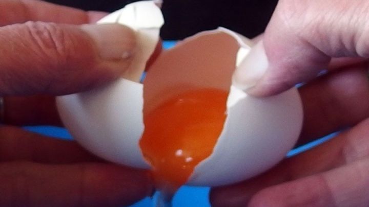 Zwei H&auml;nde brechen ein Ei auf, w&auml;hrend das Eigelb herausl&auml;uft; der Fokus liegt auf dem Aufschlagen und Trennen des Eies.