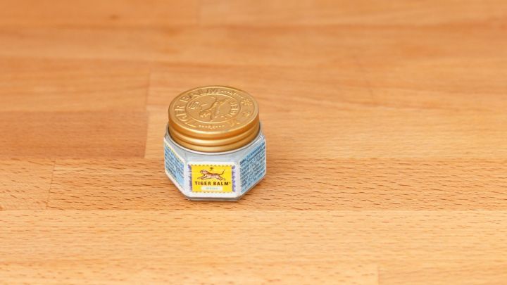 Eine kleine, sechseckige Dose mit goldener Verschlusskappe steht auf einem Holzuntergrund. Sie enth&auml;lt die Chinasalbe gegen Kopfschmerzen.