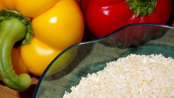 Bunte Paprikaschoten liegen neben einer Sch&uuml;ssel mit Hirse, bereit zur Zubereitung eines gesunden Gerichts.