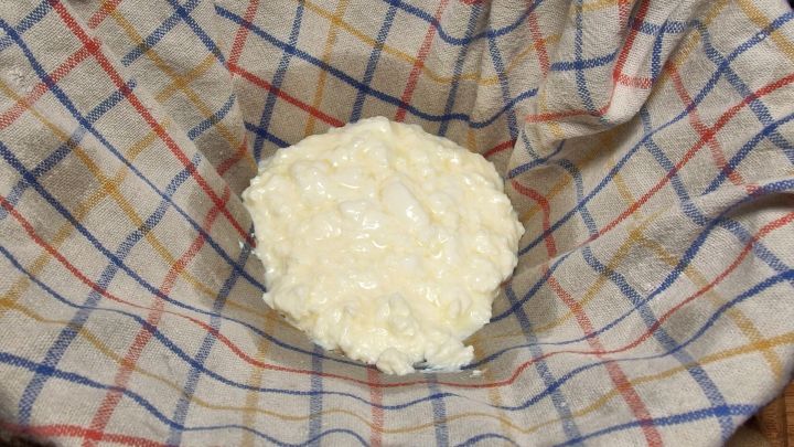 Ein frischer Quark liegt auf einem karierten K&uuml;chentuch, das zum Abtropfen verwendet wird. Die Umgebung ist heimisch und einladend.