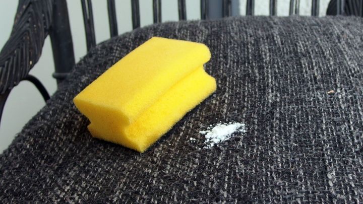 Ein gelber Schwamm liegt auf einem dunkelgrauen Polster, daneben ist etwas Waschpulver verstreut.