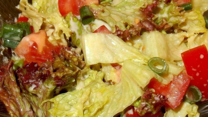 Frischer Salat liegt in einer Sch&uuml;ssel, w&auml;hrend eine fruchtige Salatsauce darauf verteilt wird, um den Genuss zu verst&auml;rken.