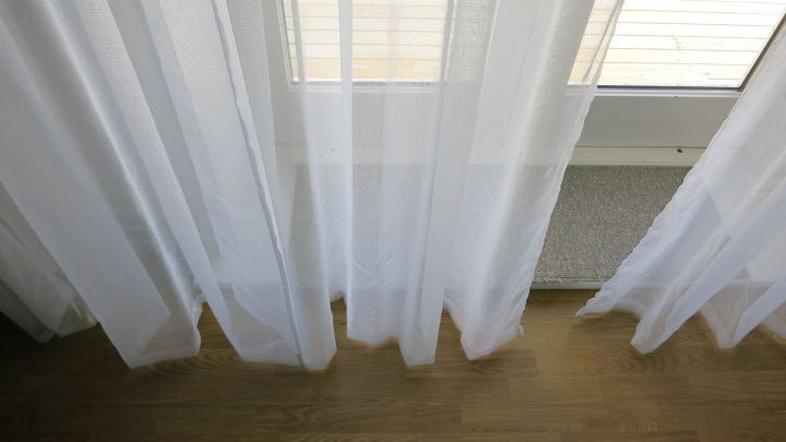 Durchsichtige Gardinen h&auml;ngen vor einem Fenster und stehen im Fokus, w&auml;hrend die Umgebung aus Holzfu&szlig;boden besteht.