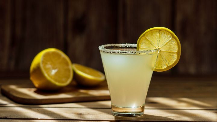 Ein erfrischendes Getr&auml;nk mit Zuckerrand und einer Zitronenscheibe steht auf einem Holztisch, umgeben von Zitronen.