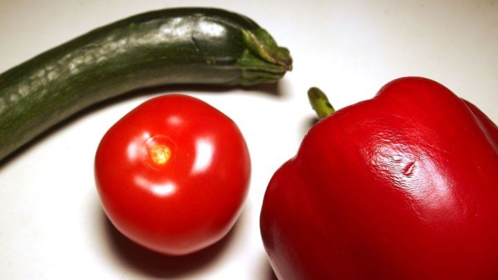 Eine gr&uuml;ne Zucchini, eine rote Paprika und eine Tomate liegen auf einer hellen Oberfl&auml;che, bereit zur Verwendung in frischen Gerichten.