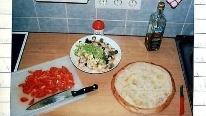 Ein gef&uuml;lltes Fladenbrot liegt auf einer Arbeitsplatte neben geschnittenen Tomaten, einem Salat mit Oliven und Oliven&ouml;l.