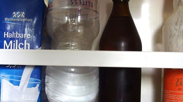 Eine ge&ouml;ffnete Flasche mit Kohlens&auml;ure steht im K&uuml;hlschrank neben einer transparenten Wasserflasche und Milch.