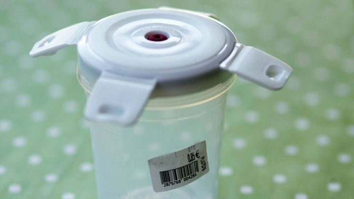 Ein transparenter Gefrierdosenbeh&auml;lter steht auf einem gr&uuml;nen Punkttisch, w&auml;hrend ein Aufkleber auf der Seite sichtbar ist.