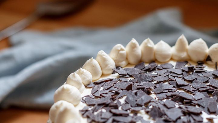 Eine Torte mit Sahne und Schokoladensp&auml;nen wird auf einem Tisch pr&auml;sentiert, umgeben von einem hellblauen Tuch.