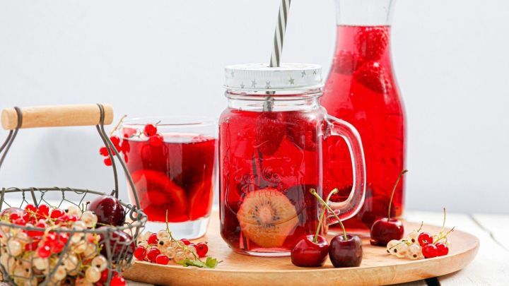 Eine bunte Kinderbowle steht auf einem Holzbrett, umgeben von frischen Fr&uuml;chten, w&auml;hrend sie in Gl&auml;ser gef&uuml;llt ist.