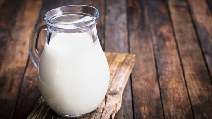 Ein Glas Milch steht auf einem rustikalen Holzbrett, das auf einer Holzoberfl&auml;che liegt.