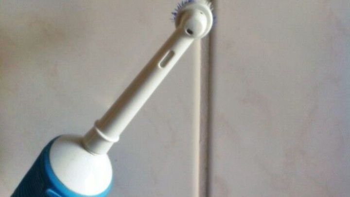 Eine elektrische Zahnb&uuml;rste reinigt Badfugen auf einer gefliesten Wand mit hellen, beigen Fliesen.