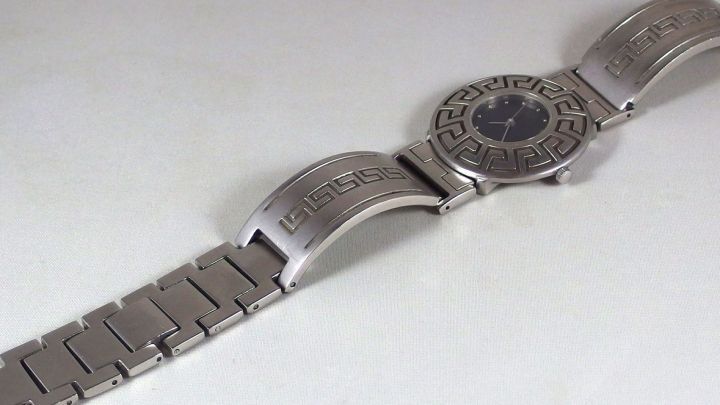 Ein Metall-Uhrenarmband wird auf einem wei&szlig;en Hintergrund betrachtet, um es mit Zahnpasta und Zahnb&uuml;rste zu reinigen.